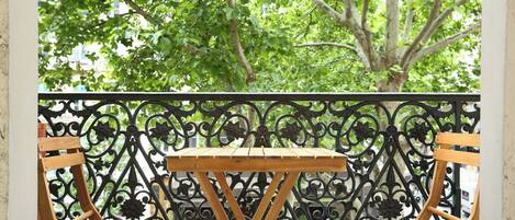 Un balcón con dos sillas de madera y una mesita, rodeado de barandillas de metal negro decorativas.