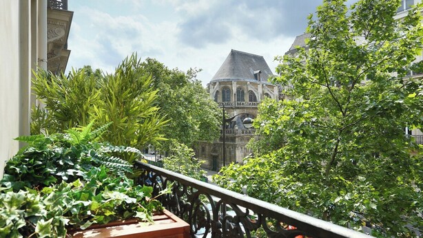 A balcony with lush greenery and a view of a historic building with a dome and arched windows. - Lovely and new Apartment Center of Paris (Paris)