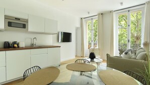 A modern kitchen with white cabinets, a flat-screen TV, and a dining area with a glass table and woven placemats. - Lovely and new Apartment Center of Paris (Paris)