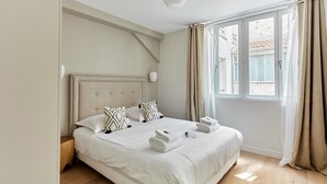 A hotel room with a large bed, a headboard, bedside lamps, a window with curtains, and a wooden floor. - Superb Apartment Porte Maillot / Arc de Triomphe (Paris)