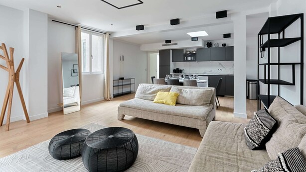 A modern living room with a sofa, black poufs, and a dining area with a table and chairs. - Superb Apartment Porte Maillot / Arc de Triomphe (Paris)