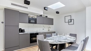 A modern kitchen with grey cabinets, a built-in oven, and a dining area with a round table set for six. - Superb Apartment Porte Maillot / Arc de Triomphe (Paris)