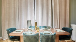 Un'area pranzo con un tavolo di legno apparecchiato per quattro persone, circondato da quattro sedie color petrolio.