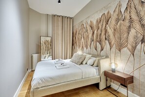 A bedroom with a large bed, a bedside table with a lamp, and a wall with a leaf pattern. - Sublim Apartment Arc de Triomphe/ Trocadero (Paris)