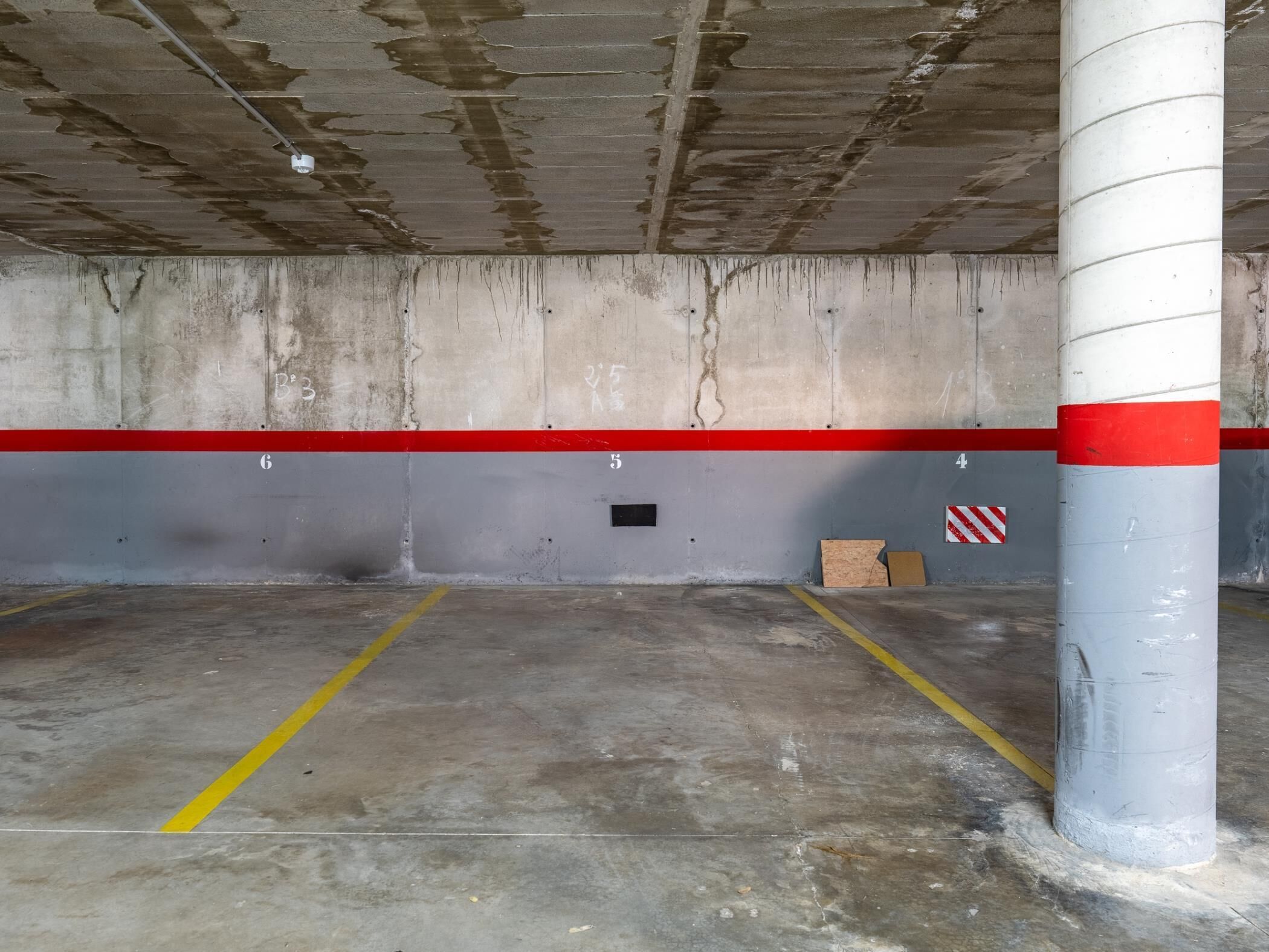 Un estacionamiento con paredes de hormigón, espacios numerados y una franja roja.