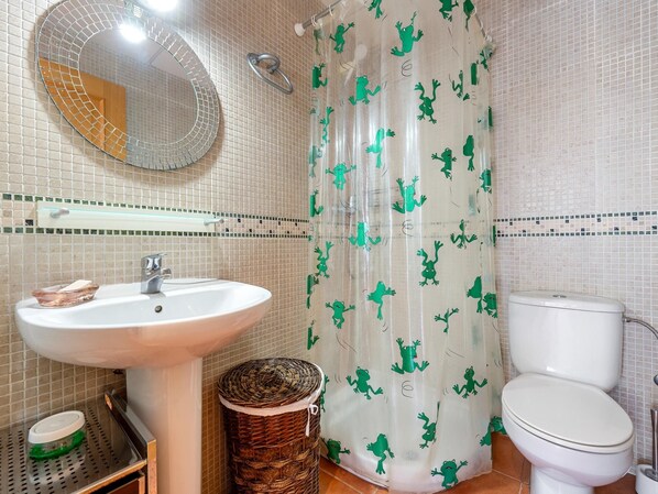 Un baño con lavamanos blanco, un espejo redondo, inodoro y cortina de ducha con estampado de ranas verdes.