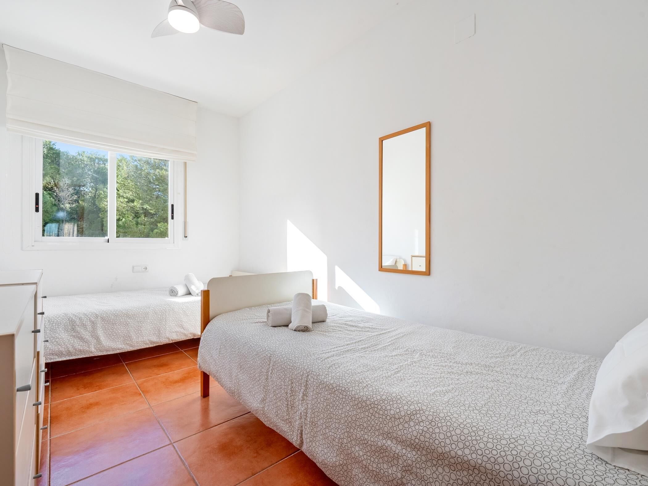 A bedroom with two beds, a large window, and a mirror on the wall.
