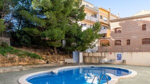 A swimming pool with a tiled deck, surrounded by a low brick wall and trees.