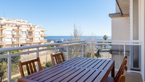 A wooden table and chairs on a balcony with a view of the sea and buildings.