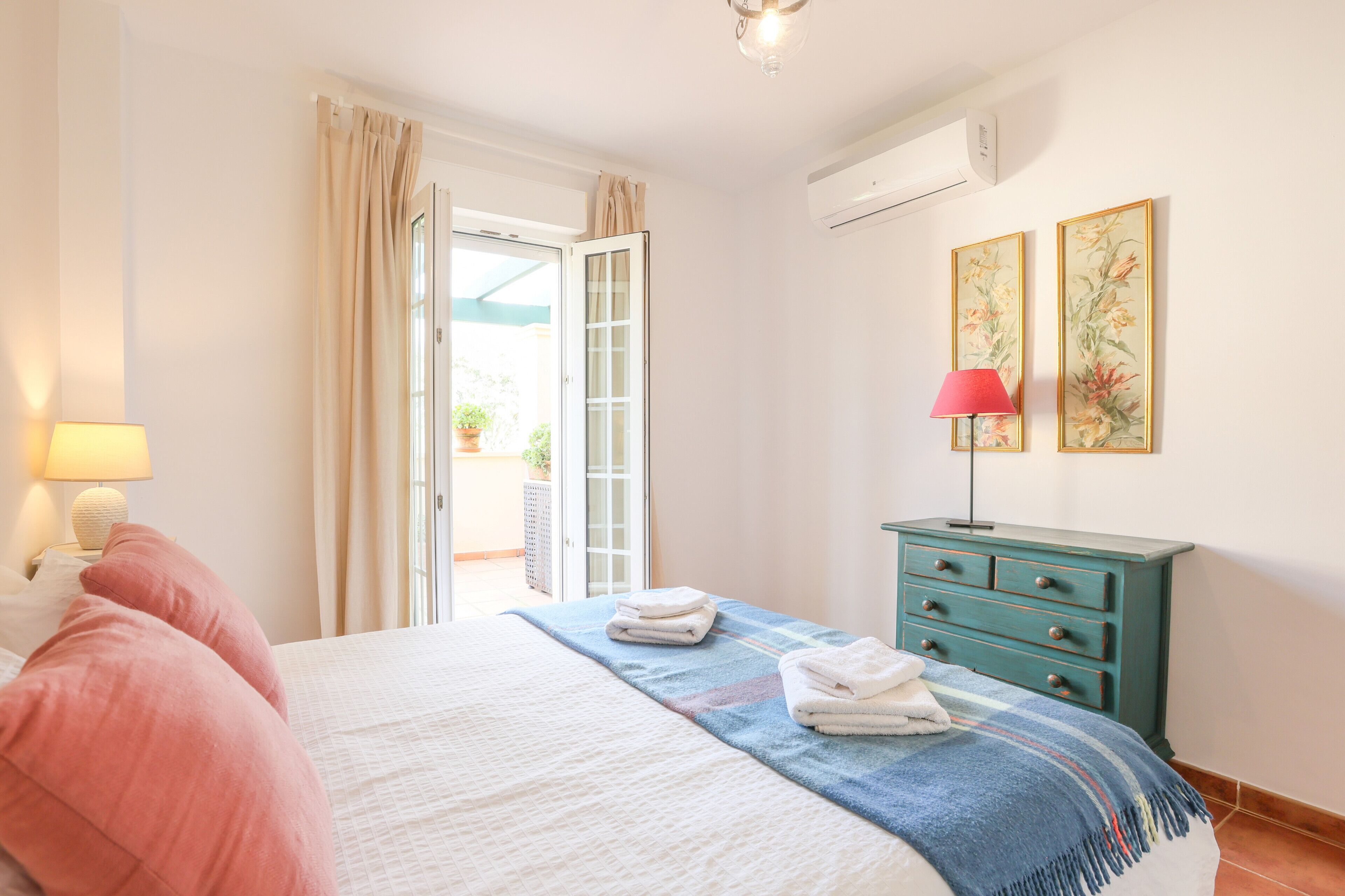 Une chambre à coucher comprenant un lit, une commode, une lampe et une porte donnant sur un balcon.