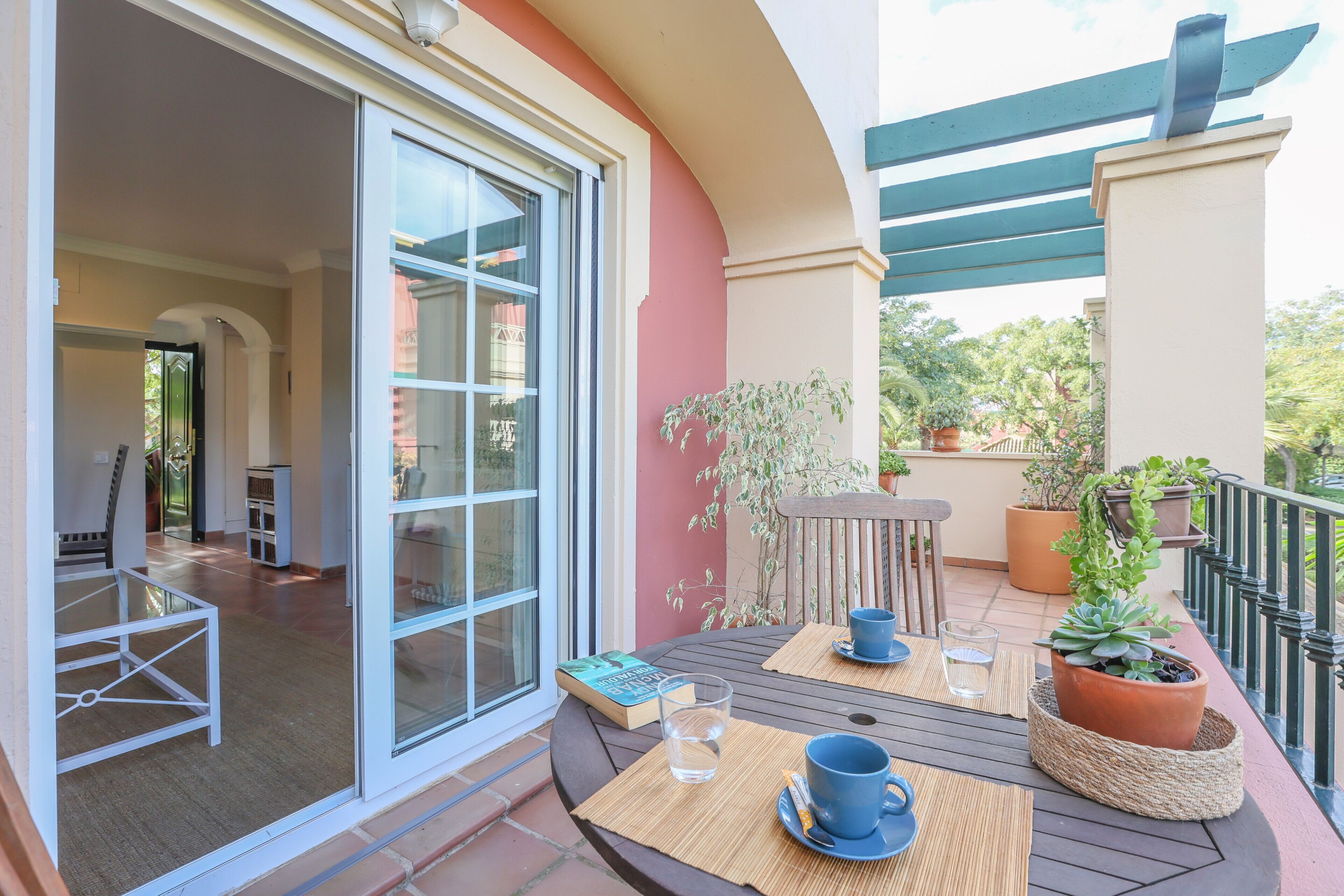 A balcony with a table, chairs, and potted plants.