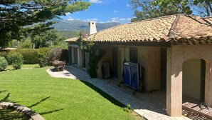 A house with a tiled roof, a patio with a table and chairs, and a view of the mountains in the background.