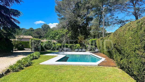 A rectangular swimming pool with a wooden deck, surrounded by well-maintained grass and various shrubs.