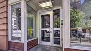 Entrada de un edificio con puertas de vidrio, un pequeño porche y vista a la calle a través de las ventanas.