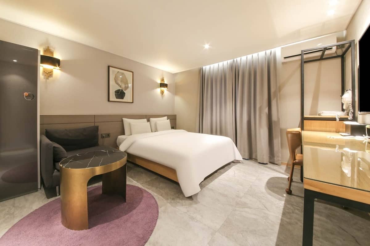 A modern hotel room with a bed, a desk, a chair, a sofa, and a small round table.
