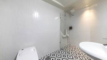 Ein Badezimmer mit weißen Fliesen, einem Boden mit geometrischem Muster, einer Dusche mit Glasabtrennung und einem weißen Waschbecken.