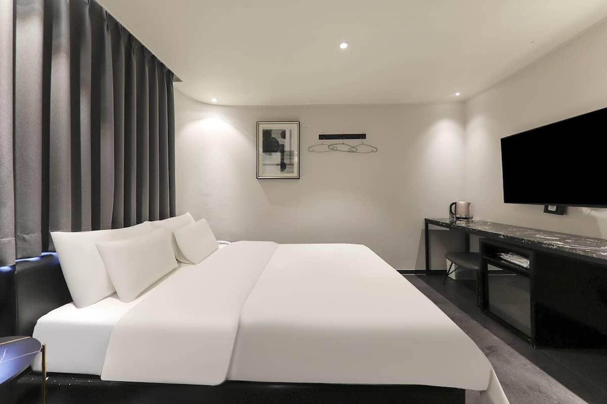 A modern hotel room with a large bed, a desk, a flat-screen TV, and a large window with curtains.