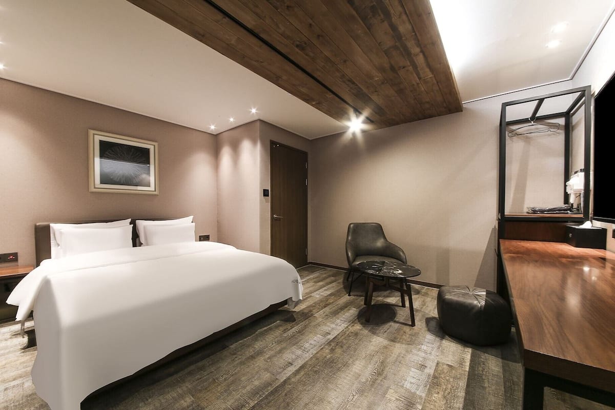 A hotel room with a large bed, a wooden ceiling, a desk with a mirror, and a chair.