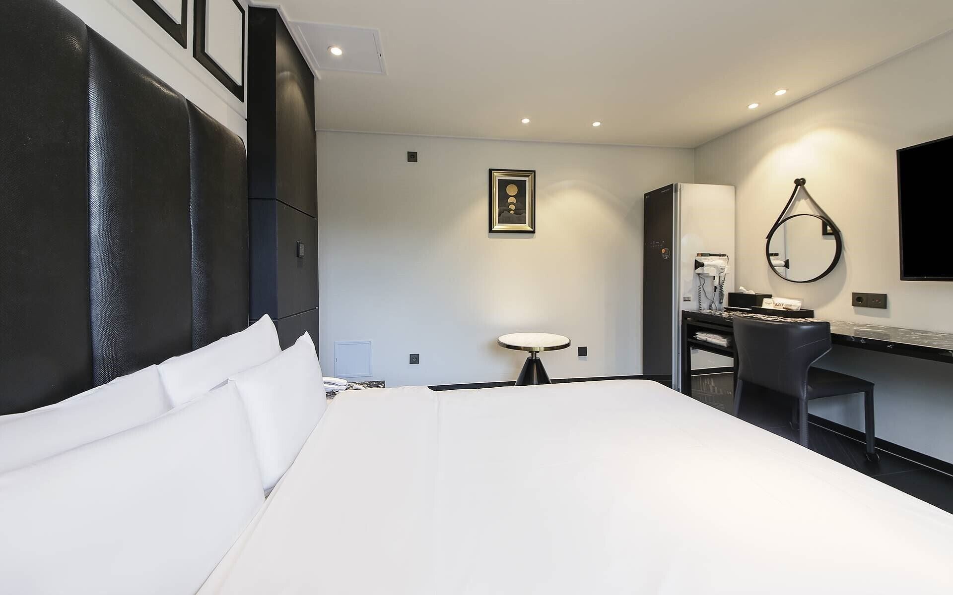 Una habitación de hotel con una cama grande, un escritorio con silla, un espejo redondo y una mesita.