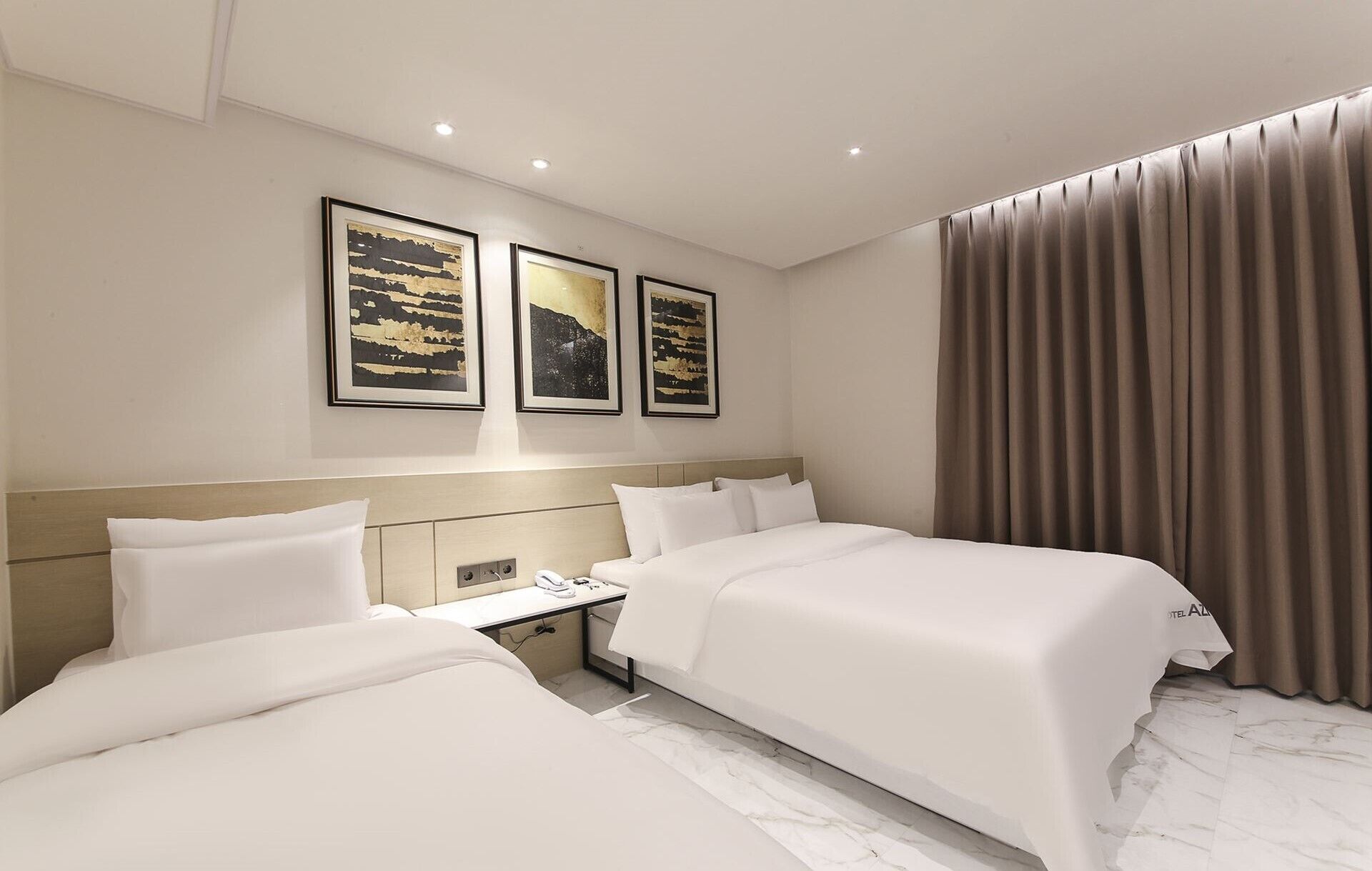 Habitación de hotel con dos camas, una mesita de noche, un teléfono y una ventana con cortinas.