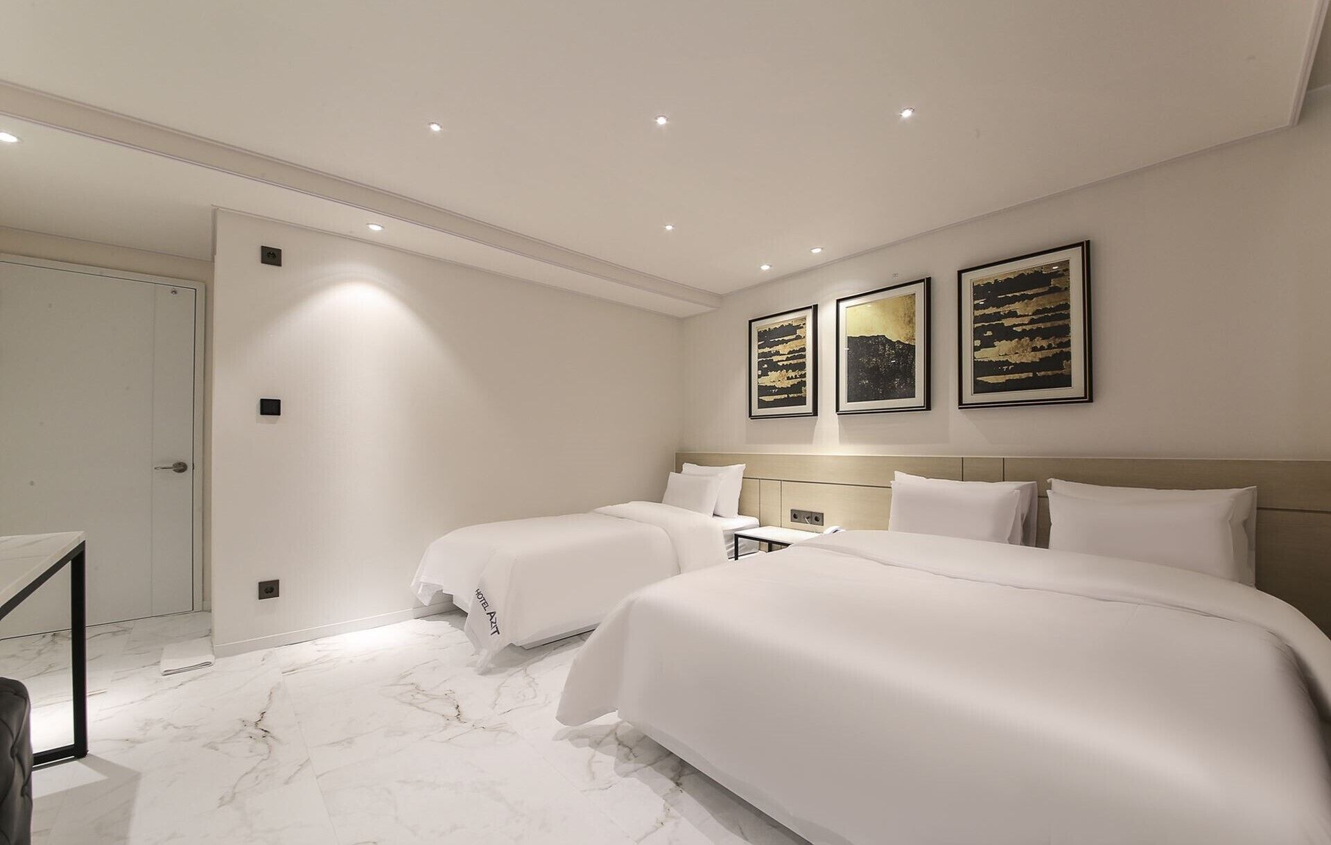 Habitación de hotel con dos camas, piso de mármol y tres obras de arte enmarcadas en la pared.
