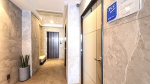 Ένας σύγχρονος διάδρομος ξενοδοχείου με μαρμάρινοι τοίχους, μια γλάστρα με φυτό και μια πινακίδα που υποδεικνύει την περιοχή για τα μέλη.