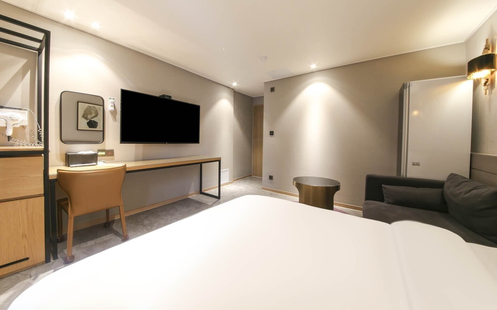 Una habitación de hotel moderna con una cama grande, un escritorio, un televisor de pantalla plana y una zona de estar con sofá.