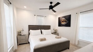 Quarto com cama, mesas de cabeceira, ventilador de teto e uma obra de arte na parede.