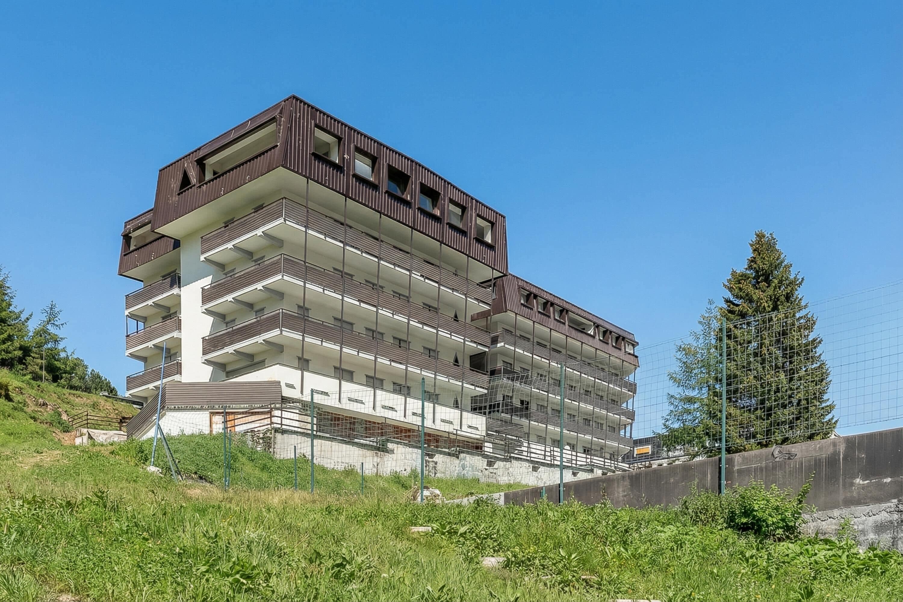 A multi-story building with balconies, a concrete base, and a surrounding fence.