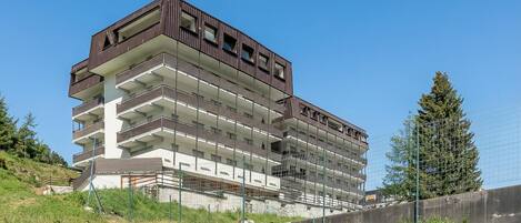A multi-story building with balconies, a concrete base, and a surrounding fence.