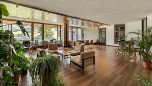 Un espace intérieur vaste et lumineux, doté d’un plancher en bois, de plusieurs coins salon et de grandes fenêtres offrant une vue sur l’extérieur.