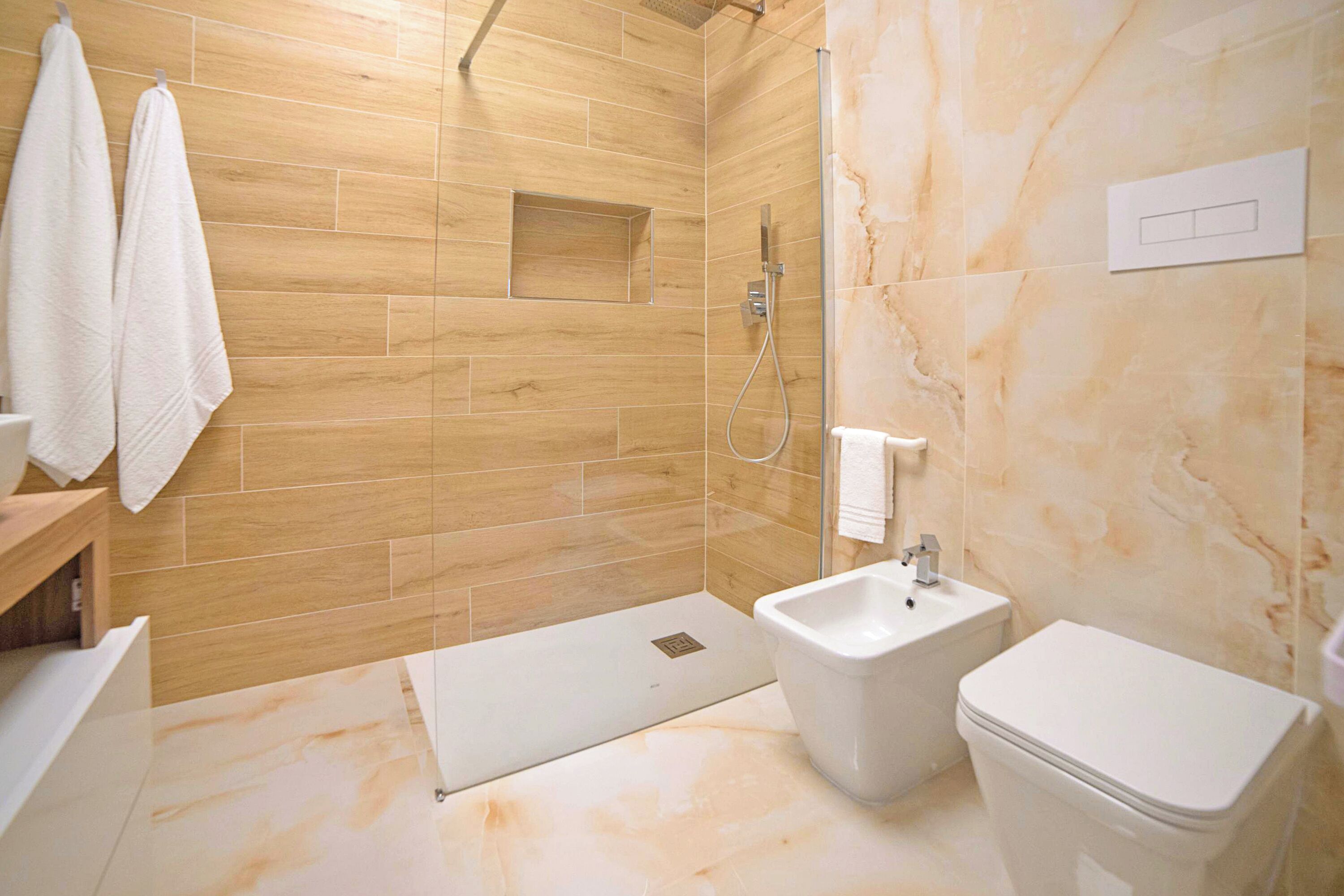 A modern bathroom with a wooden shower enclosure, a bidet, and a toilet.
