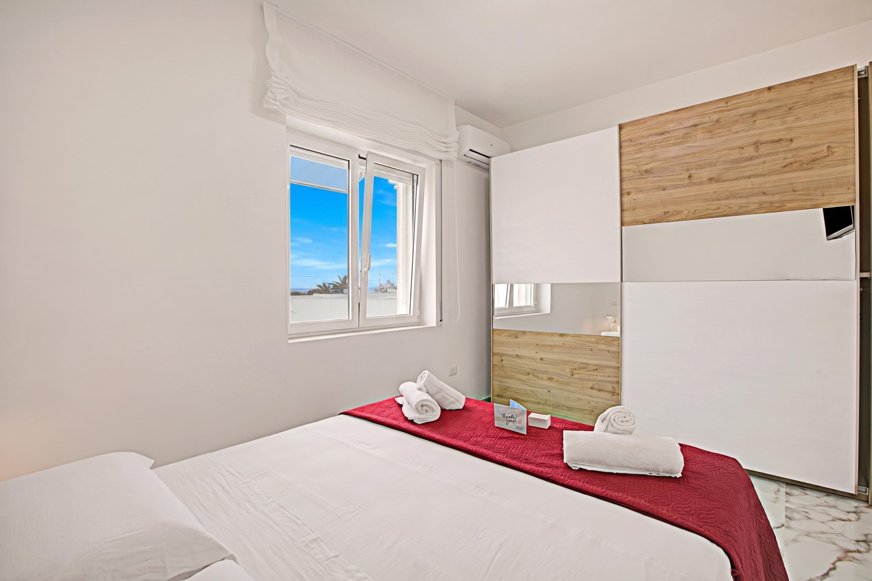 A hotel room with a bed, a window, a wooden headboard, and a mirror.