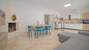 Una sala de estar moderna con un sofá gris, un comedor con mesa y sillas, y una cocina con armarios blancos y un horno empotrado.