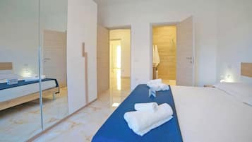 Quarto de hotel moderno com cama grande, área de estar separada e divisória de vidro.