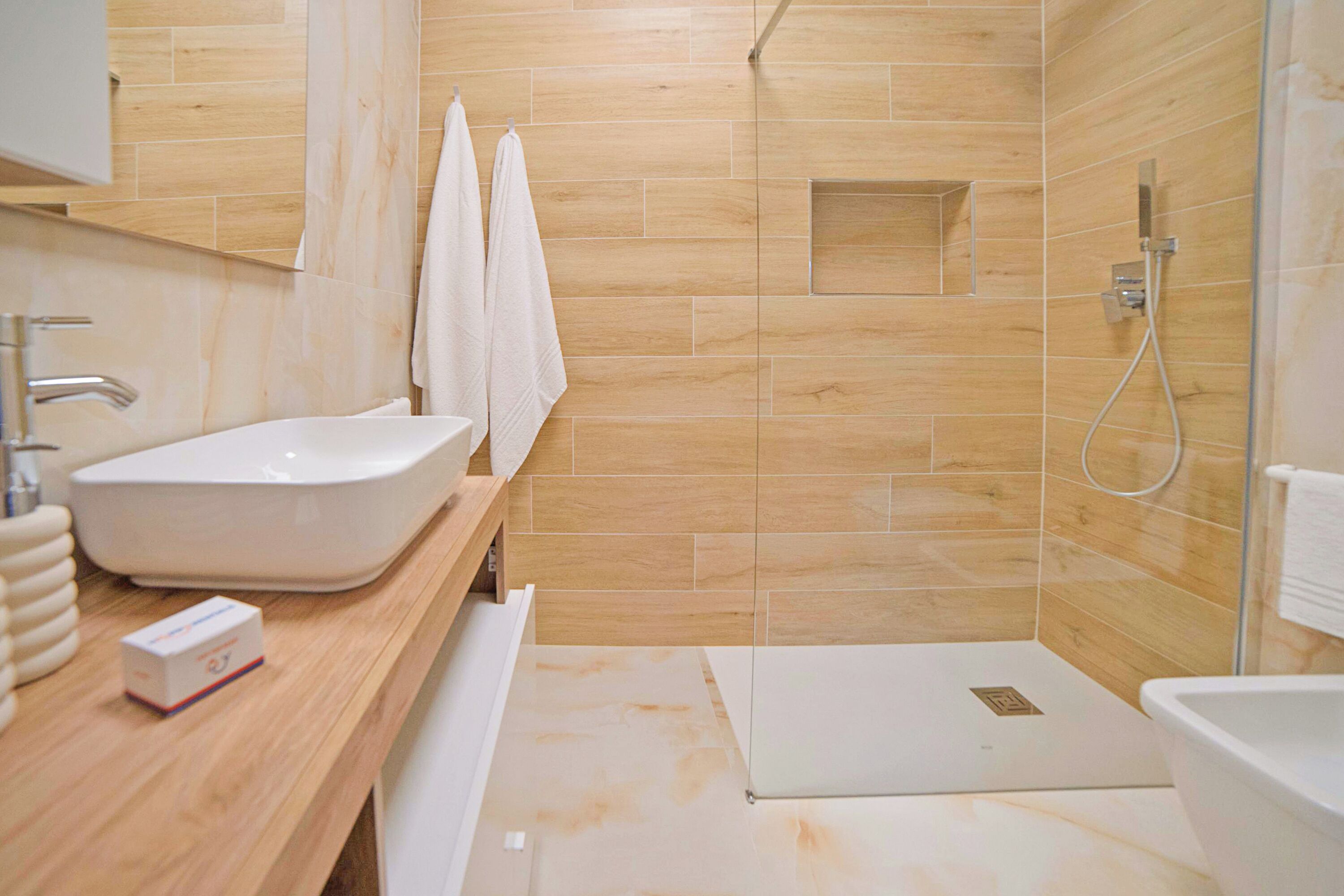 A modern bathroom with a large sink, a shower, and a mirror.