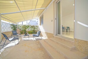 An outdoor patio area with a yellow canopy, a table with chairs, and a view of the interior through a glass door. - Villa Na' Lu' 1 With Sea View (Lecce)