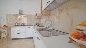 Una cocina moderna con armarios blancos, un lavamanos de acero inoxidable y un salpicadero de mármol.