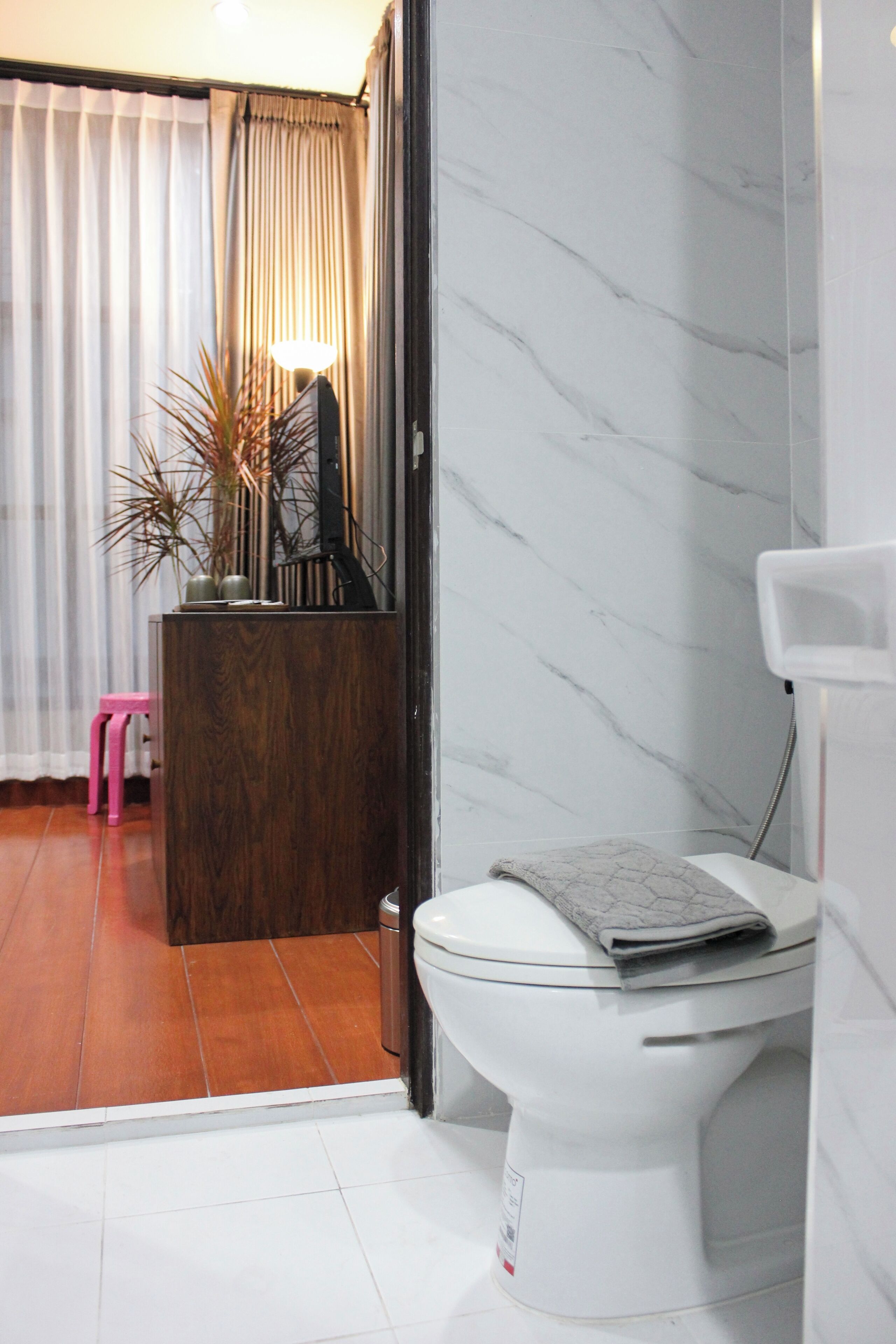 A bathroom with a toilet, a wooden vanity, a pink stool, and a potted plant.