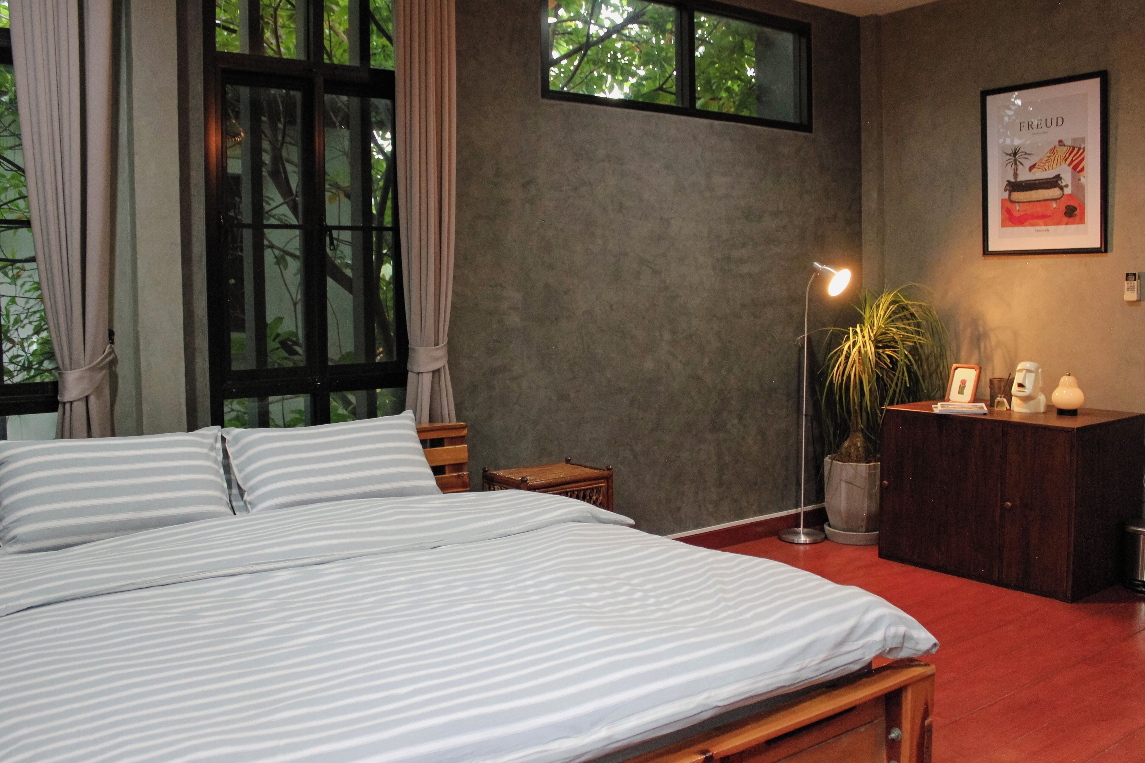 A bedroom with a large bed, a desk, a potted plant, and a framed picture on the wall.