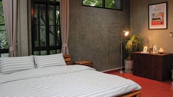 A bedroom with a large bed, a desk, a potted plant, and a framed picture on the wall.