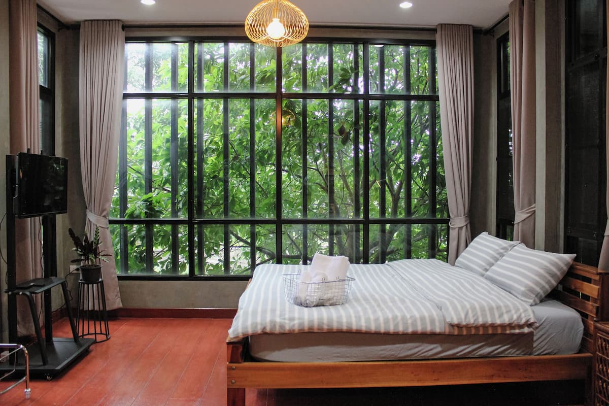A bedroom with a large window, a bed, a TV, and a treadmill.