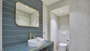 Ein Badezimmer mit gefliesten Wänden, einem Waschbecken mit goldfarbenem Wasserhahn, einer Toilette und einem Spiegel.