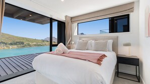 A bedroom with a large bed, a nightstand, a lamp, and a view of a lake and mountains.