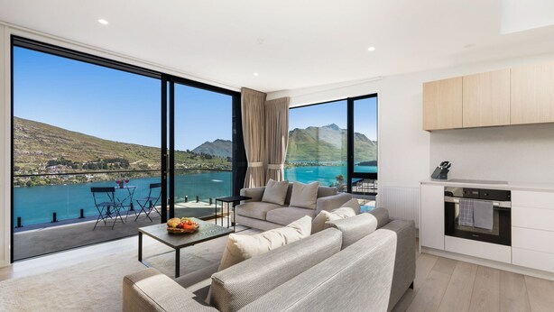 A modern living room with a large sofa, a coffee table with fruit, and a view of a lake and mountains.
