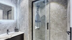 A modern bathroom with a glass-enclosed shower, a white sink, and a dark-toned vanity. - Sublim Apartment Arc de Triomphe/ Trocadero (Paris)