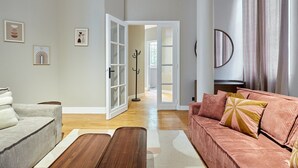 A living room with a beige sofa, a pink sofa, and a wooden coffee table. There is a coat rack and a mirror on the wall. - Sublim Apartment Arc de Triomphe/ Trocadero (Paris)
