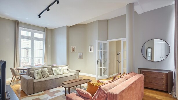A spacious living room with a sofa, a coffee table, and a television. There is a large window providing natural light and a view of the outside. - Sublim Apartment Arc de Triomphe/ Trocadero (Paris)