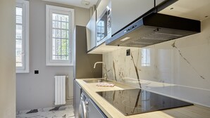 A modern kitchen with a marble countertop, a built-in oven, and a window with a view of greenery.