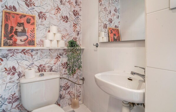 Un baño con inodoro, lavabo y espejo. El papel tapiz presenta diseños florales y hay una pequeña planta en maceta en la pared.